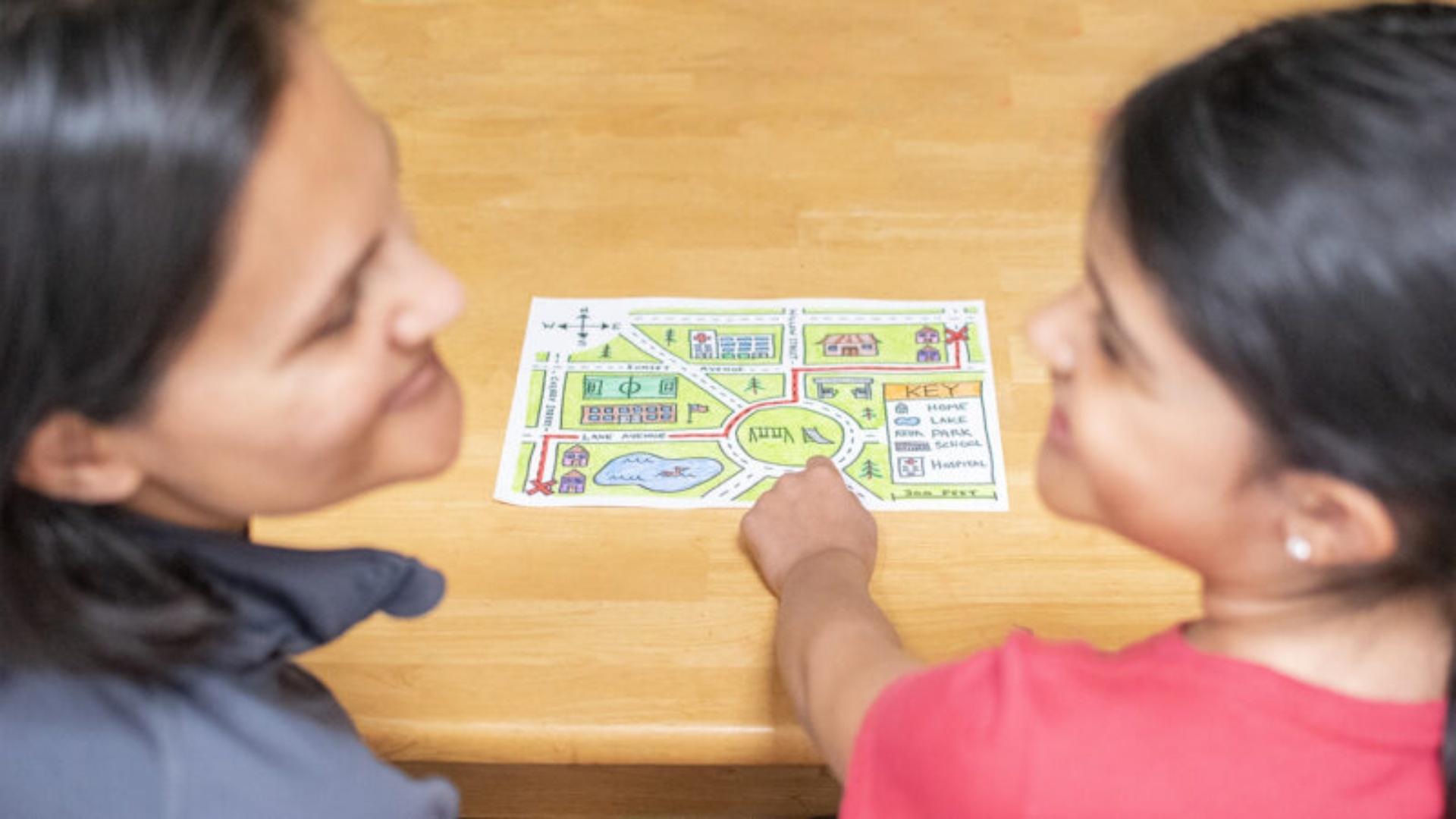 A homemade map on an oak colored table, a parent and a child looking at each other.