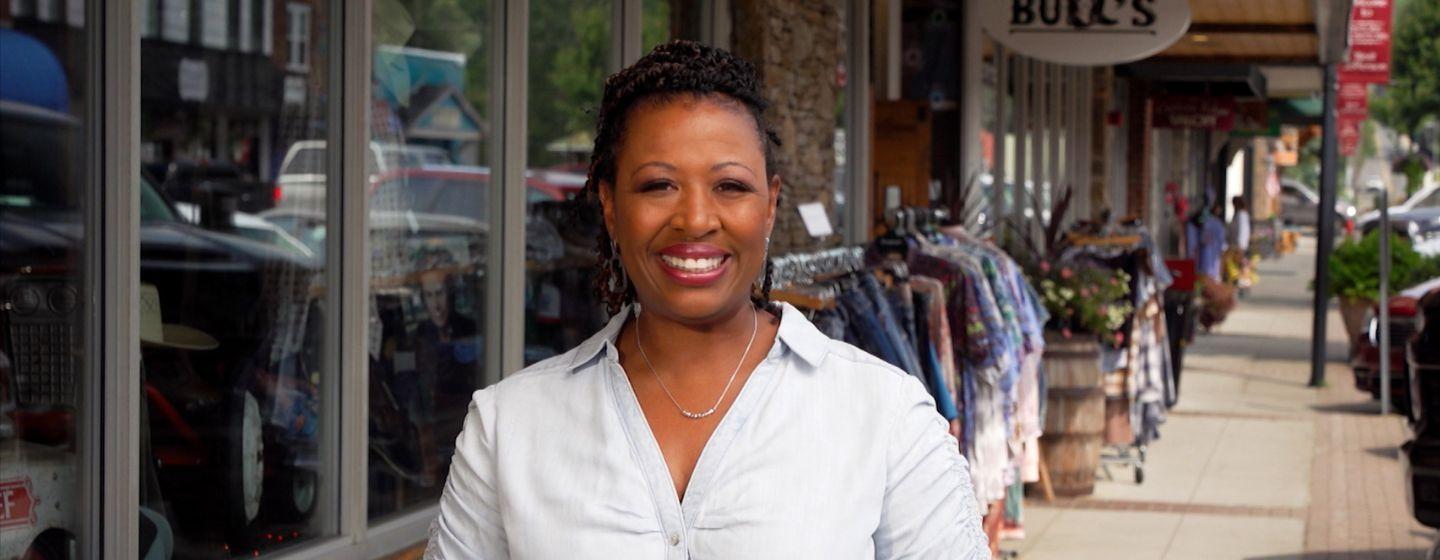 Deborah Holt Noel stand on a sidewalk in front of some shops.