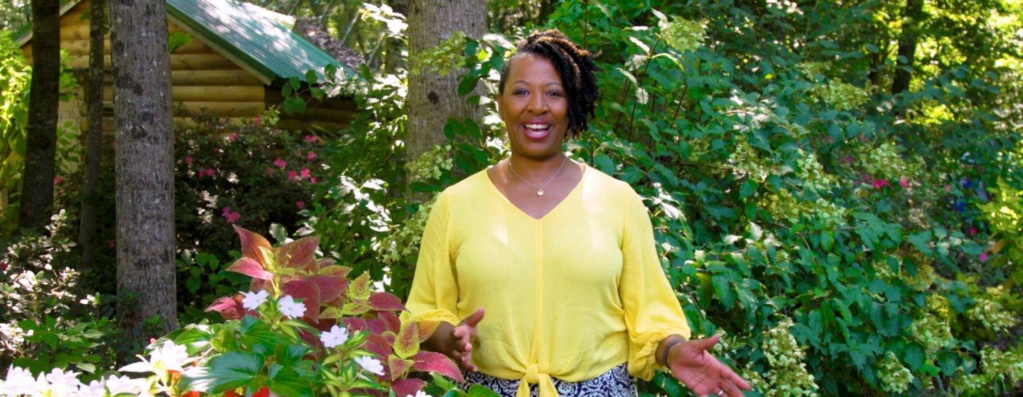 Deborah Holt Noel Talking outside by a flowery bush.