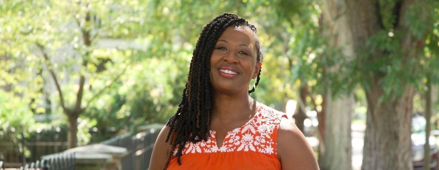 Deborah Holt Noel, host of NC Weekend with an orange tank top on smiling.