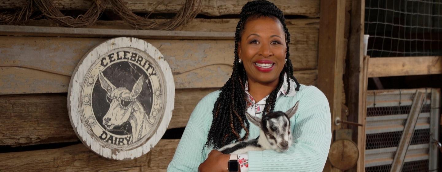 Host of NC Weekend Deborah Holt Noel holding a baby goat with a "Celebrity Dairy" sign behind her.