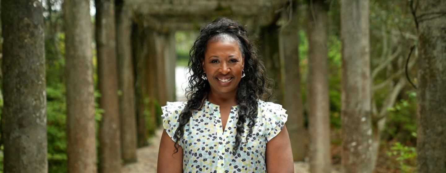 A photo of Deborah Holt Noel standing on a path with wooden columns.