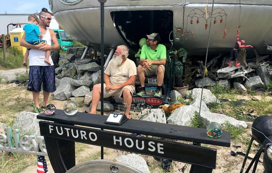 Two men, James Bagwell (left) and Leroy Reynolds sit on the steps leading into the Frisco UFO. They greet a man holding a child, visiting the site.