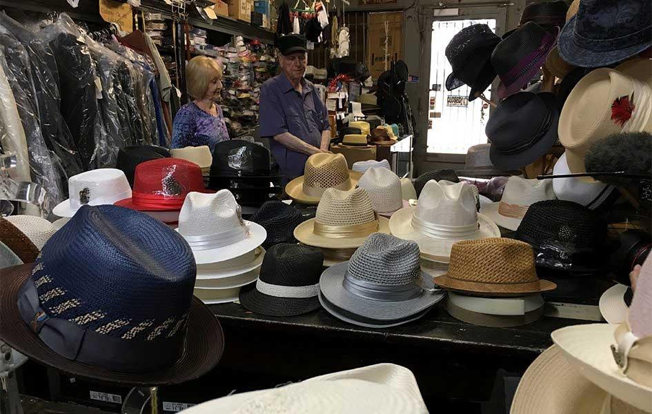 large selection of hats sitting on display table with man and women in background looking at floor
