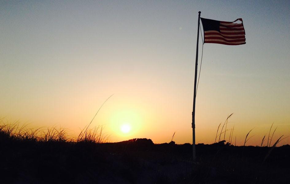 United States flag on sand dune with sun setting in background