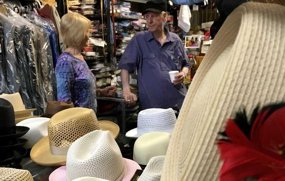 John Mitchell drinking coffee and standing with his wife in his store with clothing and hats displayed throughout
