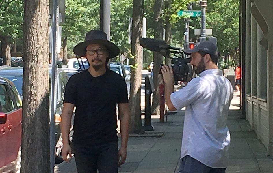 Joe Kwon walks down a street in Raleigh while cameraman Matt Maisano films a close up.