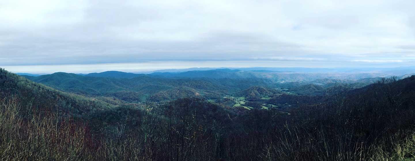 view from a mountain overlooking green mountains and cloudy skies
