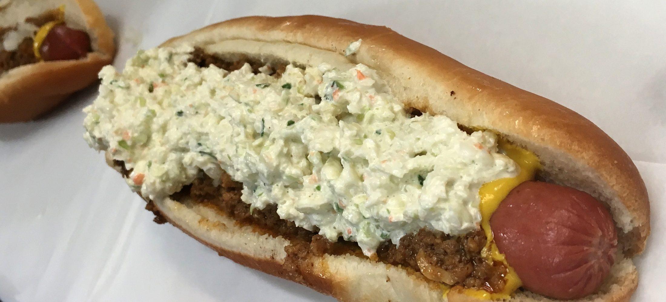 Hot dog in white bun placed on white background. Hot Dog is covered in slaw, and mustard