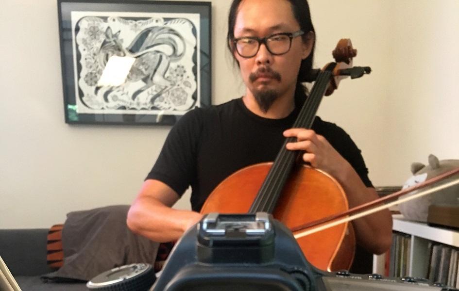 Joe Kwon sits in a room playing his cello.