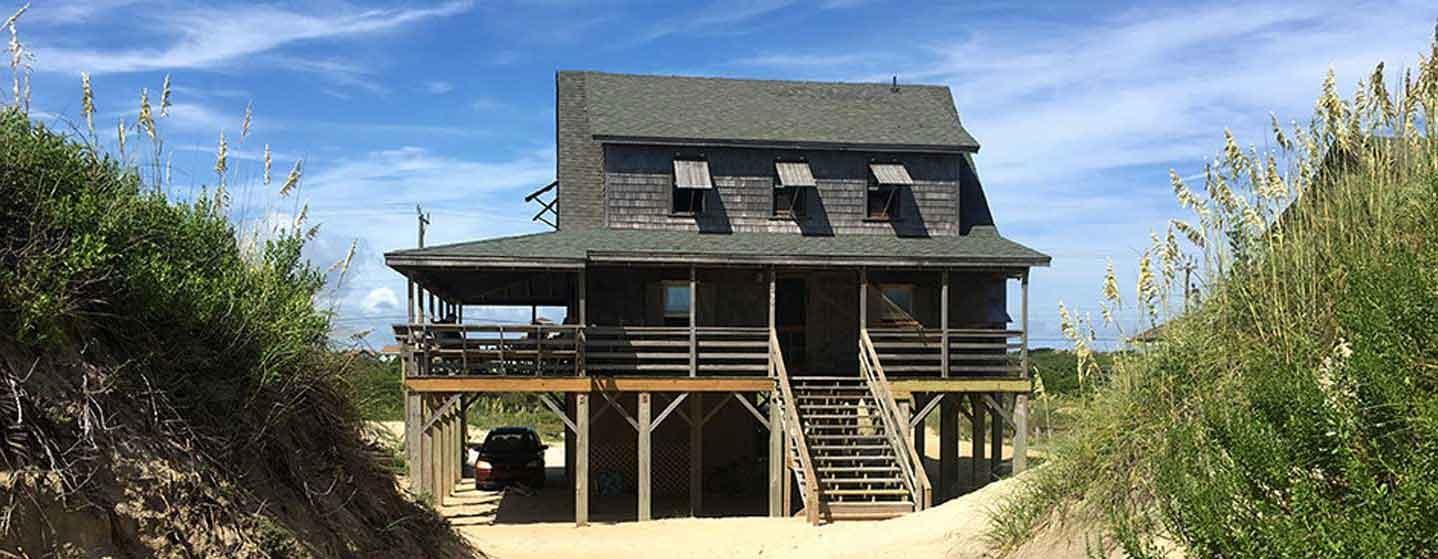 wood and shingled beach house with sand dunes on sides and sky in background