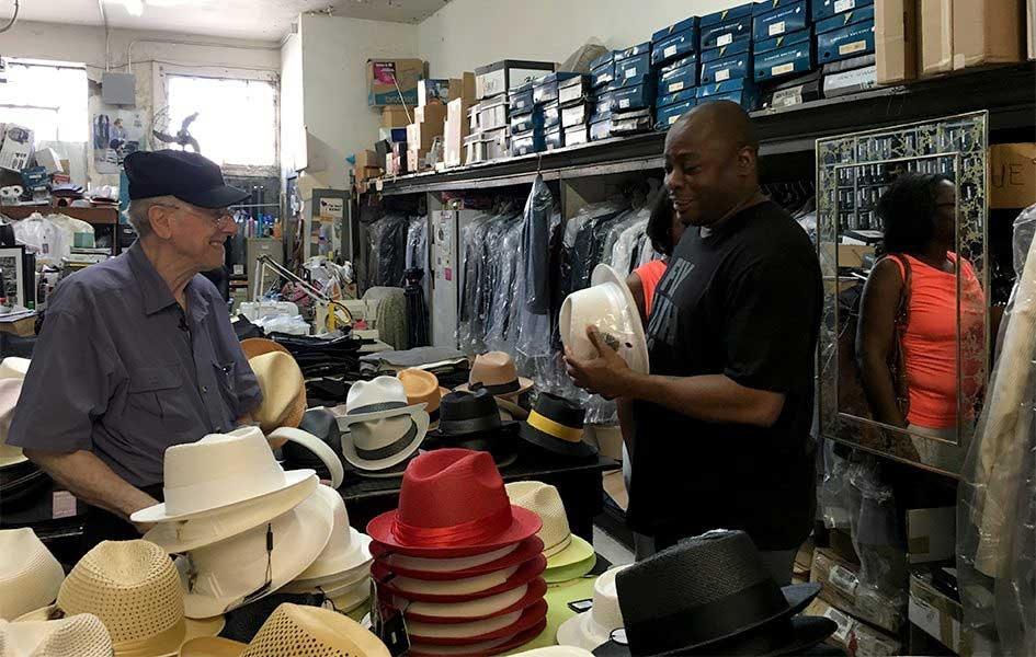 John Mitchell smiling while helping customer holding a hat