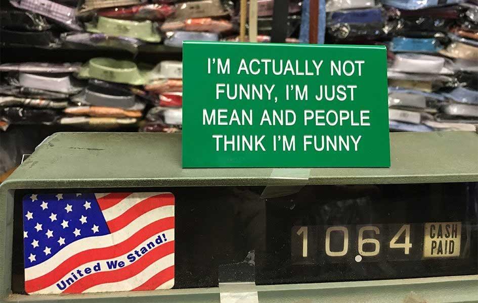 Green sign with the words "I'm actually not funny, I'm just mean and people think I'm funny" sitting on antique cash register inside a clothing store
