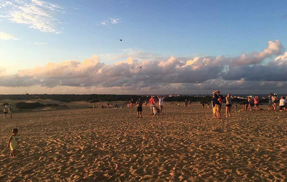 large sandy area with groups of people standing together and cloudy sky in background