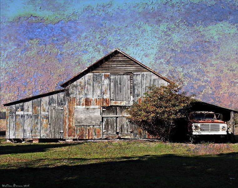 A older rusted building, to the side of it holds a red pickup truck