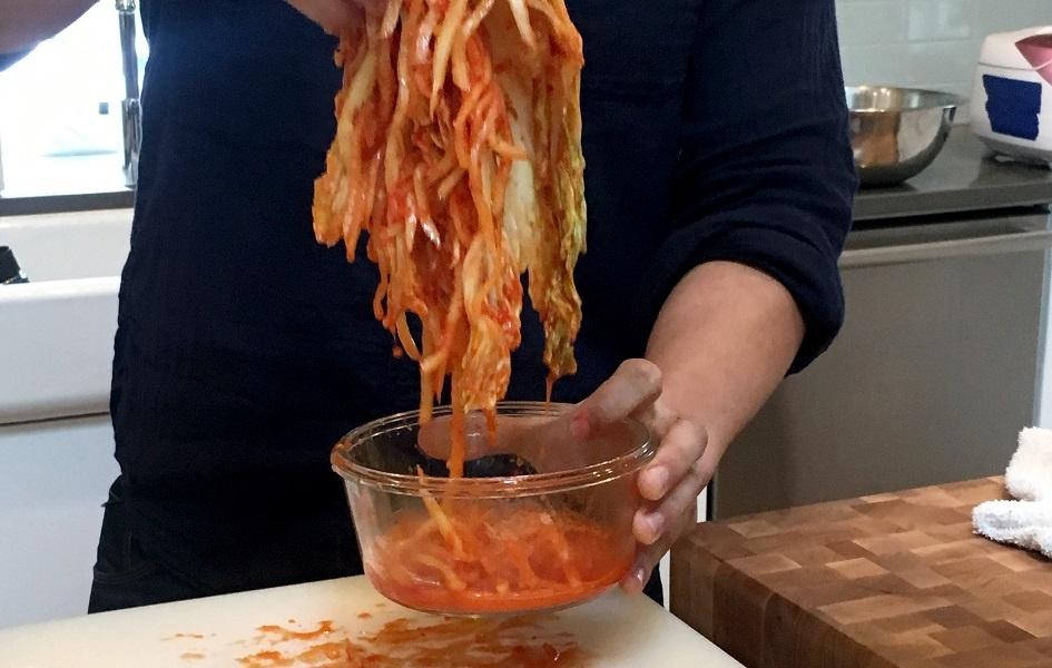 A close up of Joe Kwon's hands as he pulls Korean kimchi out a glass bowl.