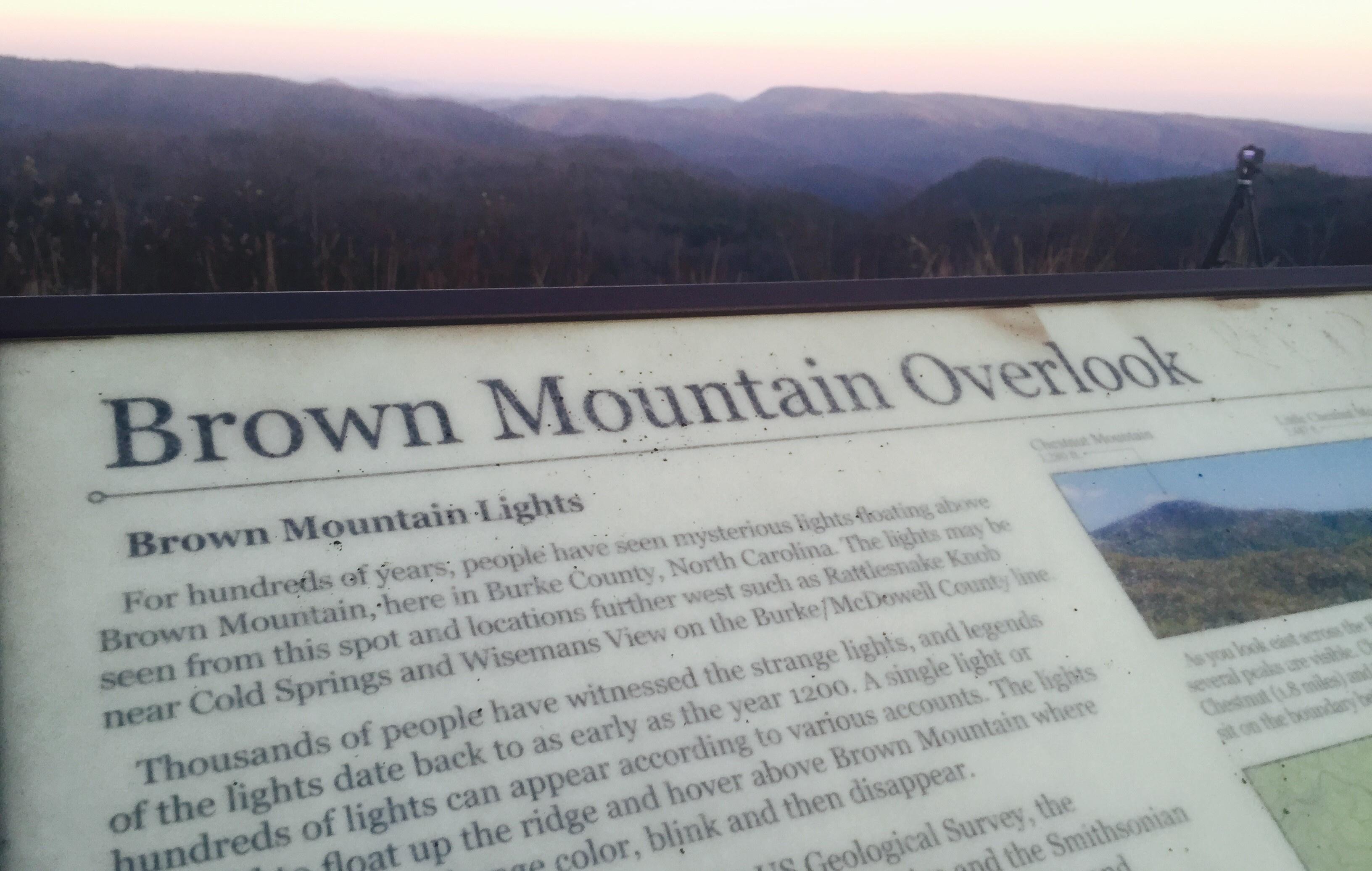 A photo of a mounted infographic with the title "Brown Mountain Overlook". Following is blurry text explaining the history of the mountain lights.
