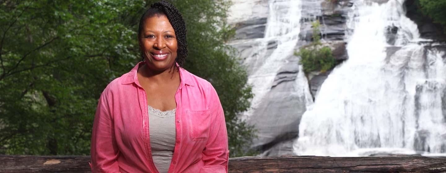 Host Deb Holt Noel smiling in front of waterfall