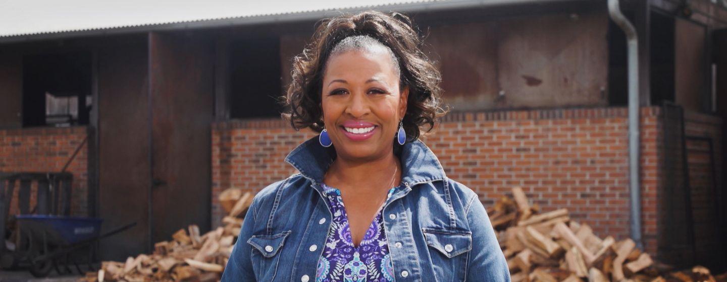 Deborah Holt Noel smiles for the camera as she wears a purple patterned top and jean jacket