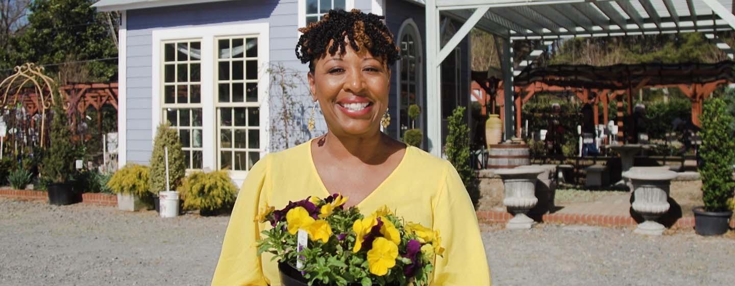 Host Deb Holt Noel smiling at the camera holding a pot of yellow and purple flowers