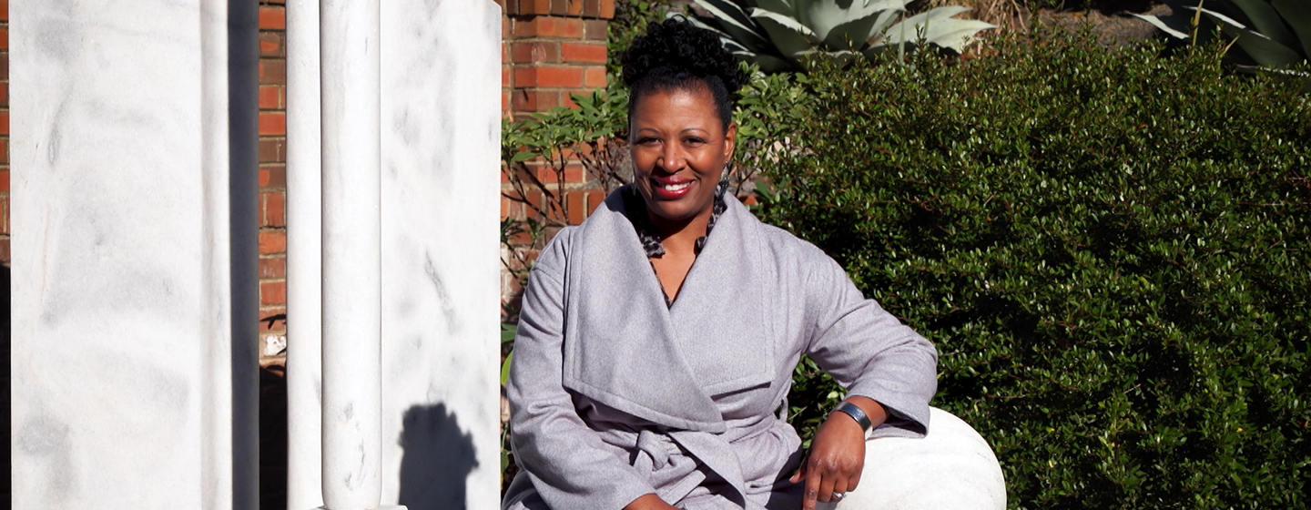 Host Deb Holt Noel sitting on white marble bench smiling