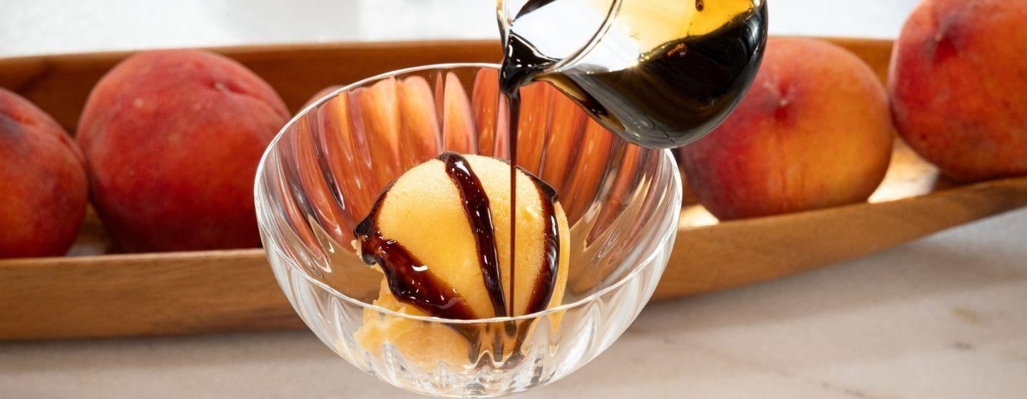 A dish of peach sorbet while a dark brown topping being poured over it.