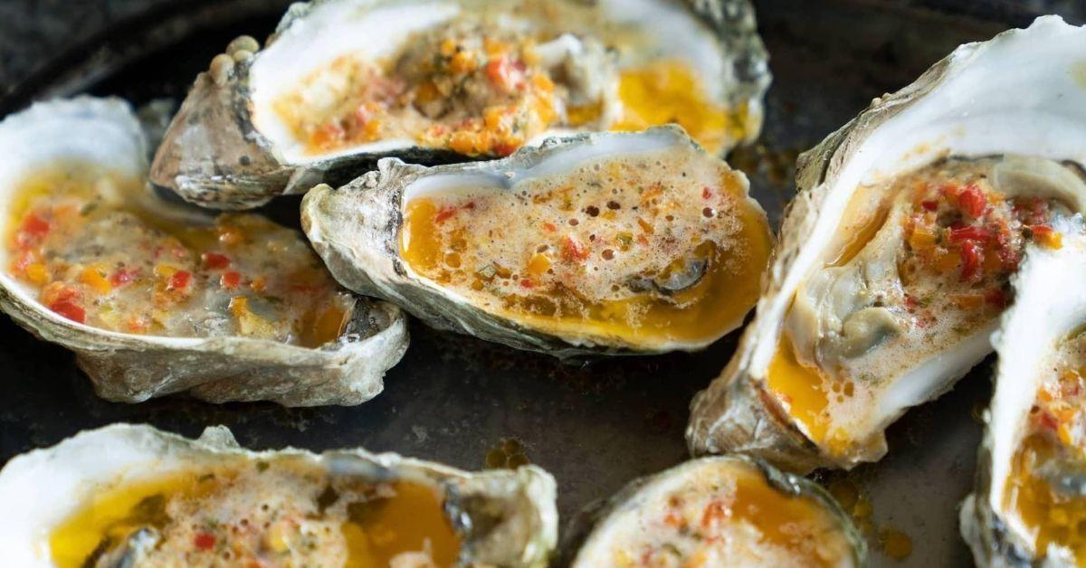 Several roasted oysters on a dark surface.