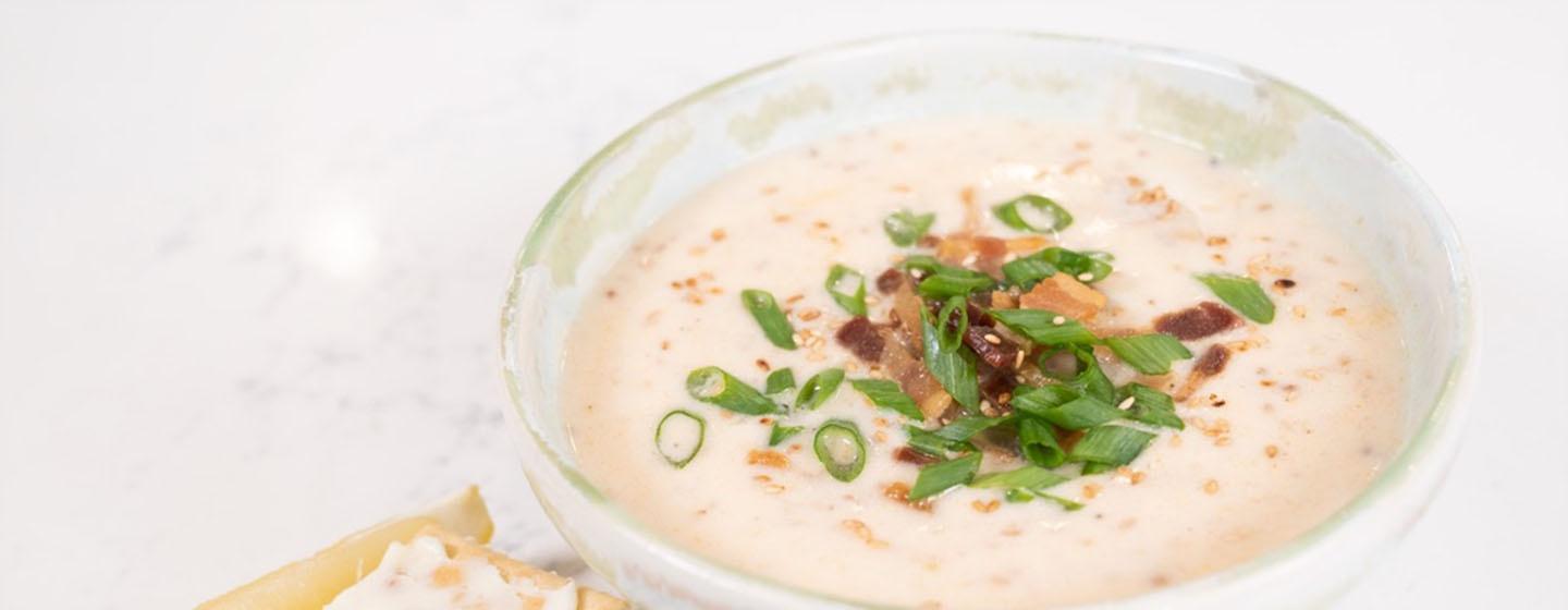 Closeup of oyster stew with toppings and crackers to the side