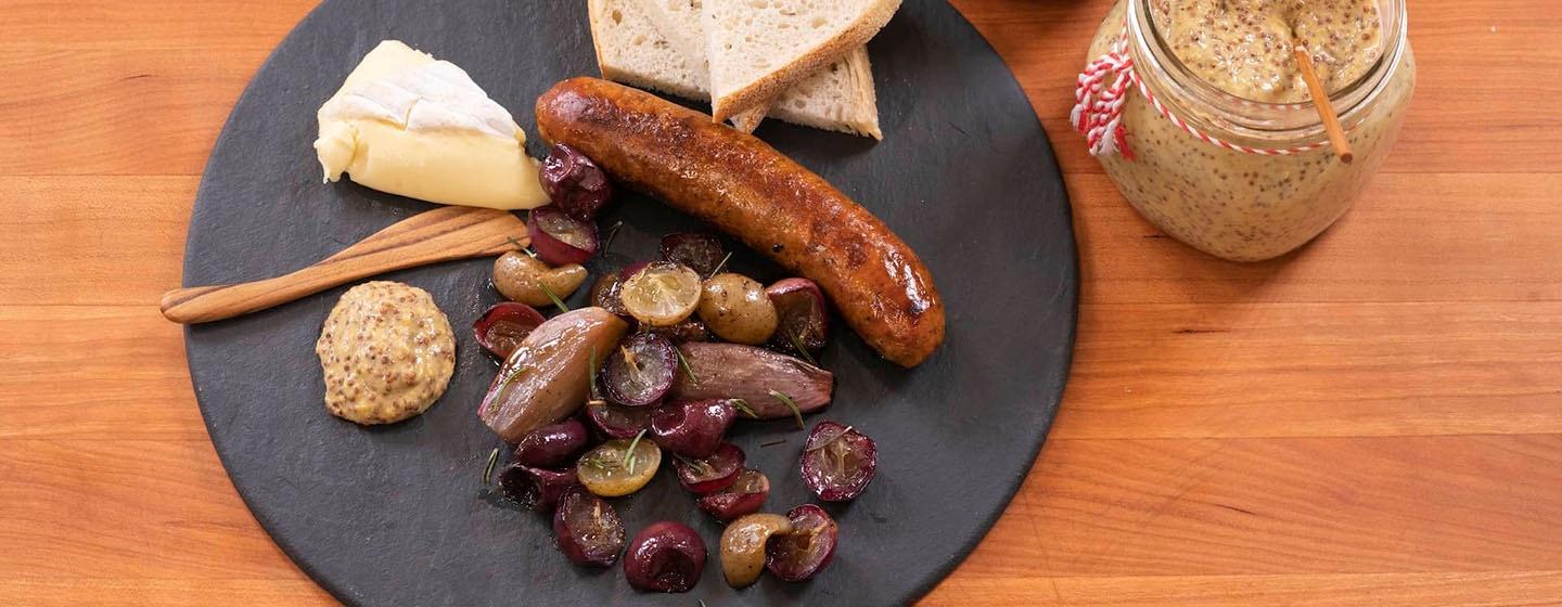 A sausage on a black plate next to bread and roasted shallots