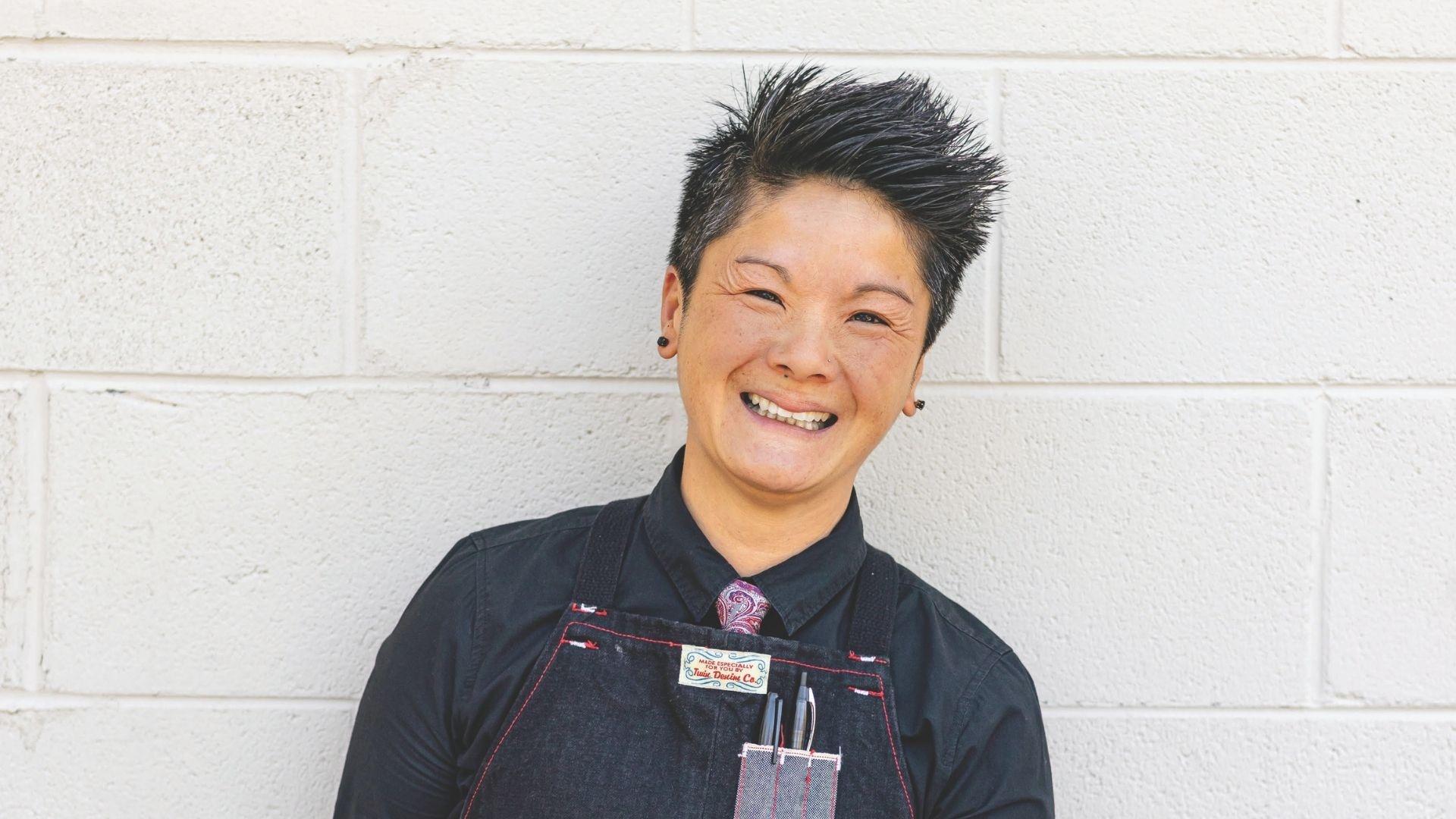 J Chong smiling in front of a white wall.