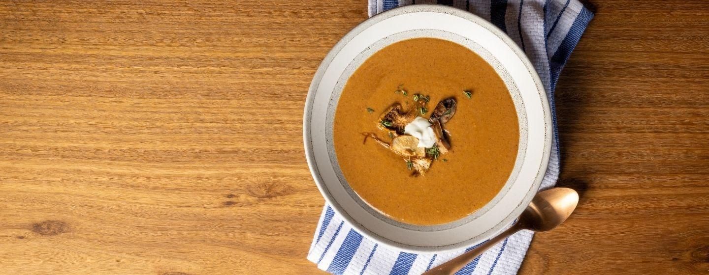 Double mushroom soup in a ceramic bowl presented on blue and white striped napkin with a bronze spoon.