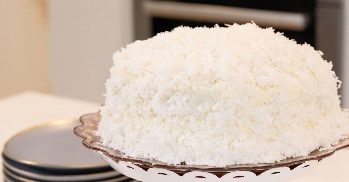 A coconut layer cake with a layer of coconut shavings covering it on a platter.