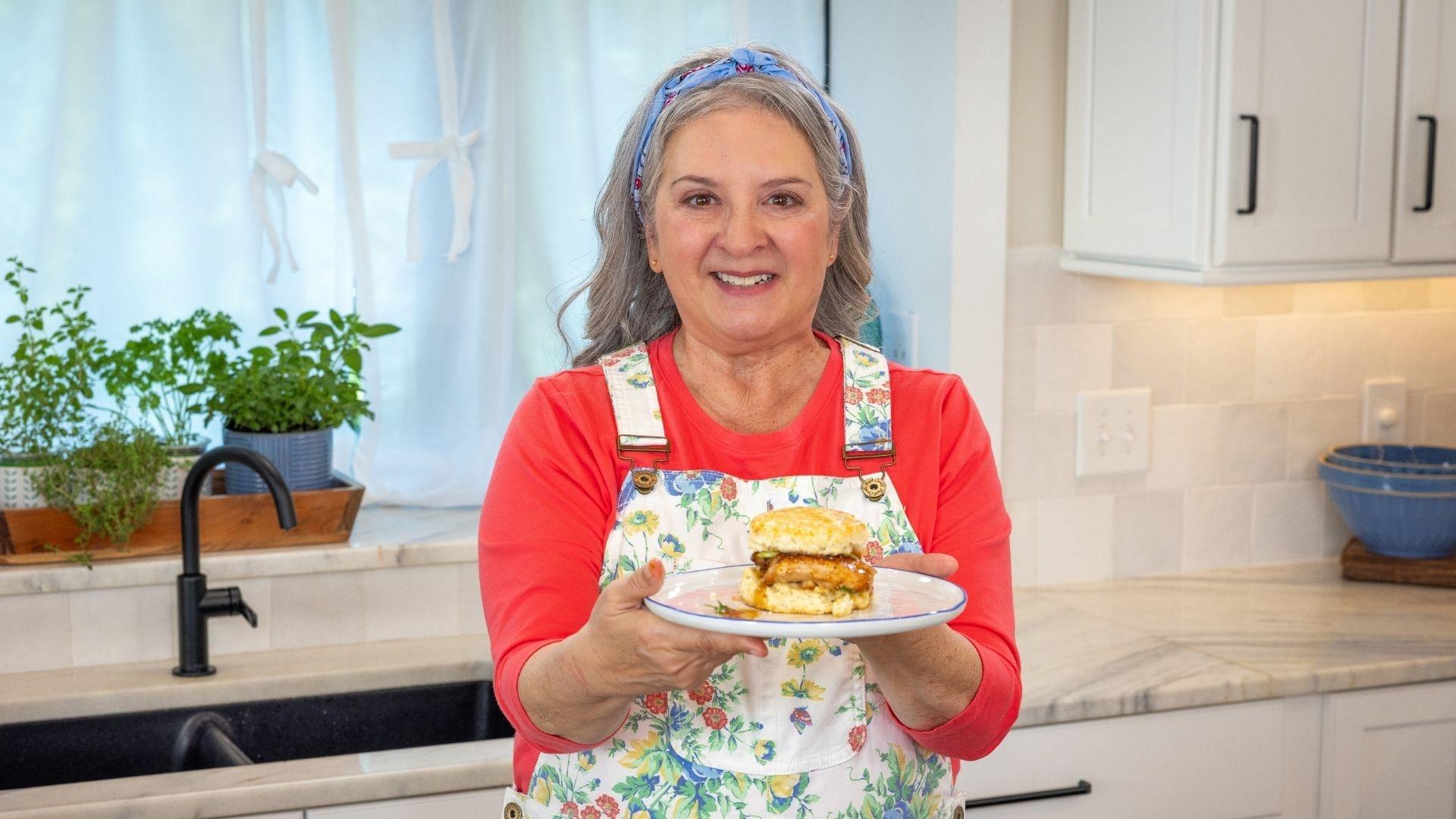 Sheri Castle holding up a cast iron pan of honey-glazed chicken.