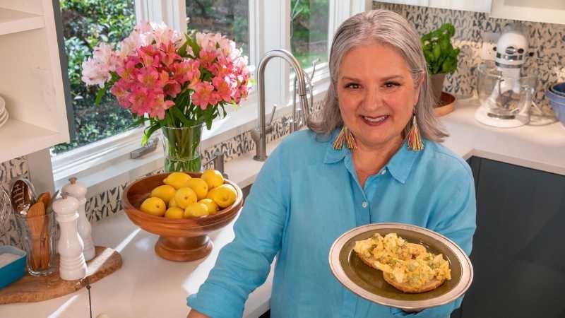 Sheri Castle holds a plate of deviled egg salad on bread in a brightly lit kitchen