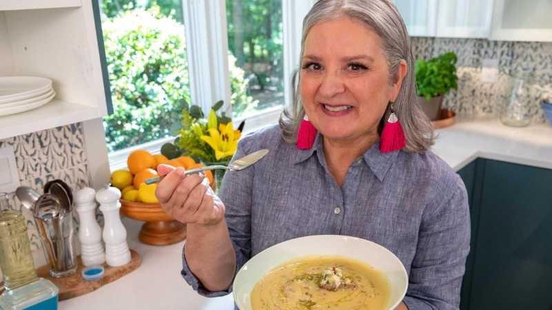 Sheri Castle holds a bowl of trout and potato soup in her left hand a spoon in her right while standing in a beautiful kitchen