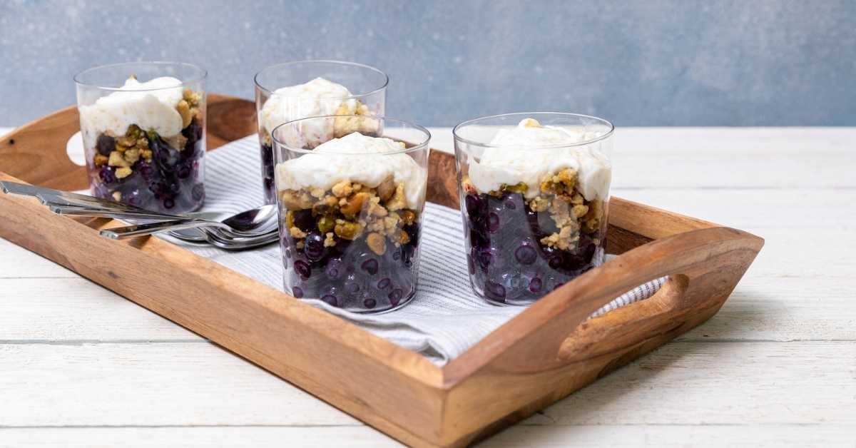 A wooden tray with four individual blueberry parfaits