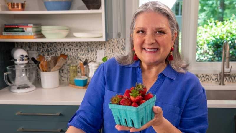 Sheri Castle wears a bright blue button-up shirt and holds a pint container of bright red strawberries