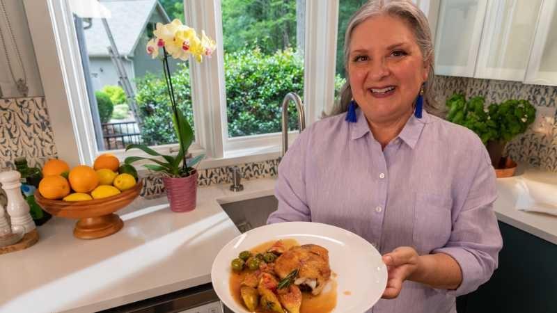 Sheri Castle presents a plate of her crispy chicken thighs with fig pan sauce in a beautiful and sunlit kitchen.
