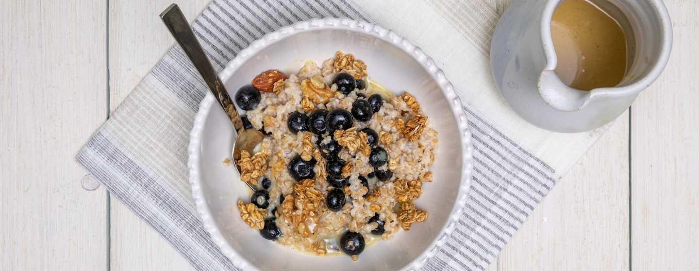 A bowl of blueberry-topped granola porridge with a small container of maple cream next to it