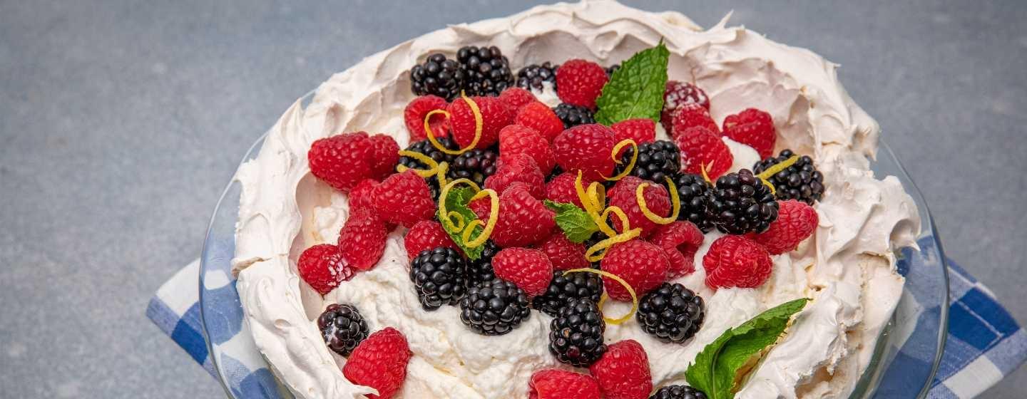 Lemon angel pie topped with fresh blackberries, raspberries, lemon zest and mint leaves sits atop a blue and white checked cloth