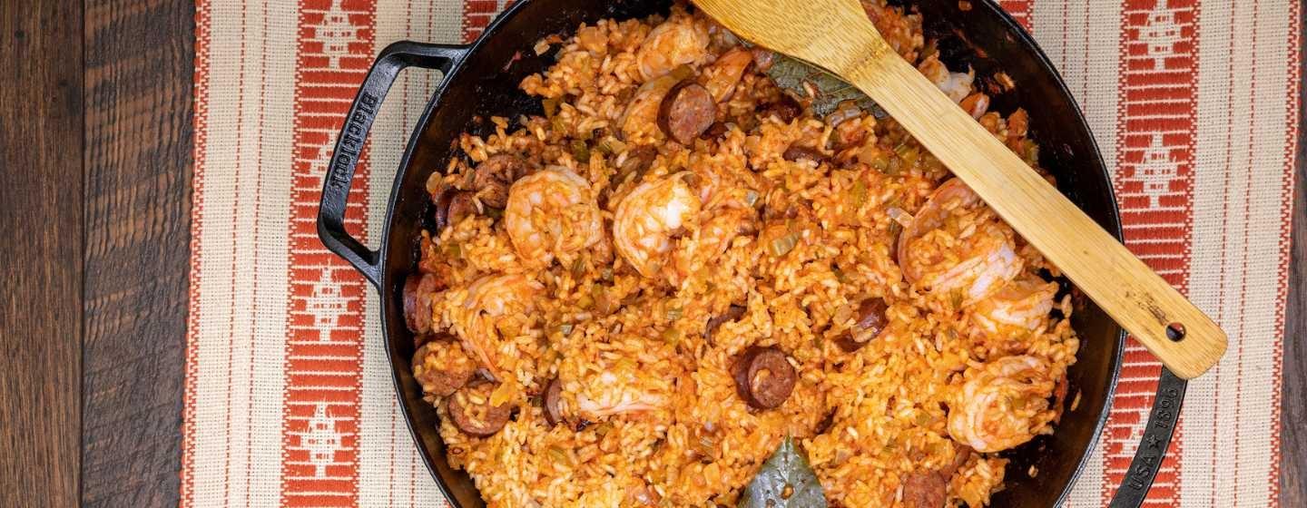 A dark bowl filled with red rice with shrimp and smoked sausage