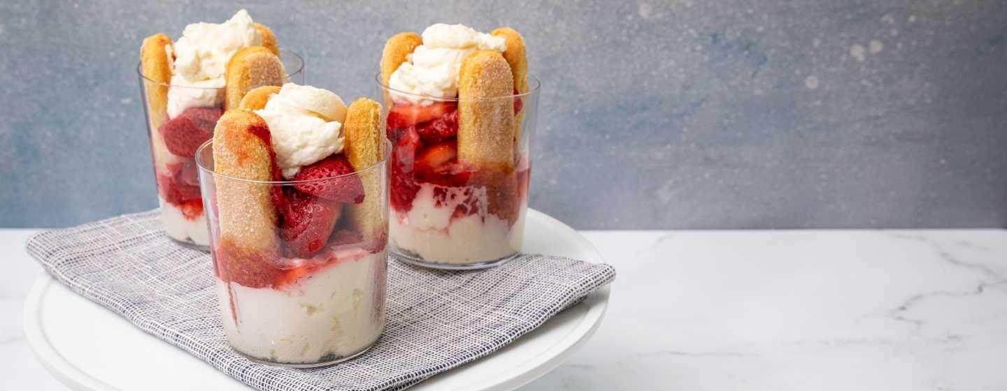 Three individual strawberry trifles are plated on a shite plate with a gray napkin