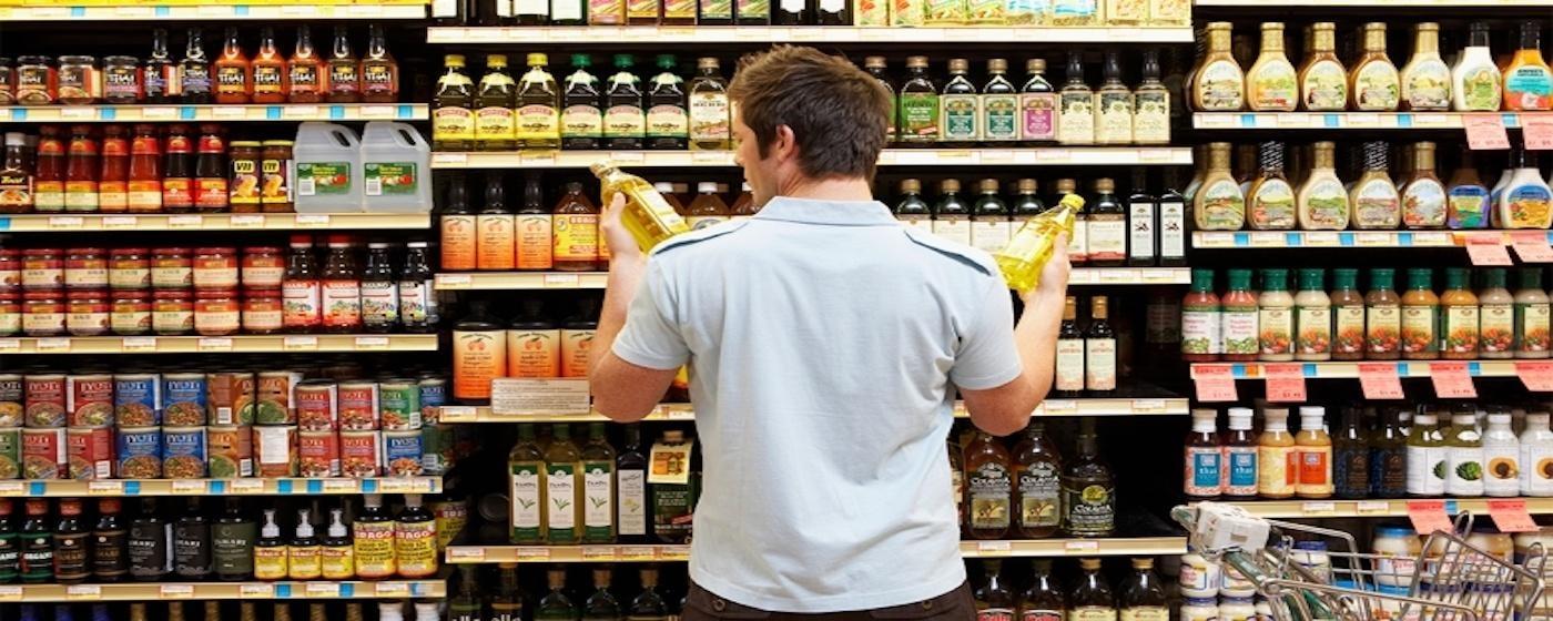 man making decision at super store holding two bottles of vegetable oil