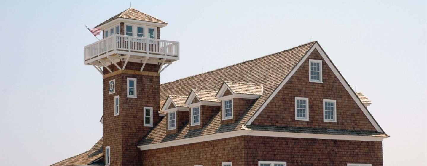 The Oregon Inlet Life-Saving Station is a large brown cape house with a watch tower attached, sitting on a beach dune.