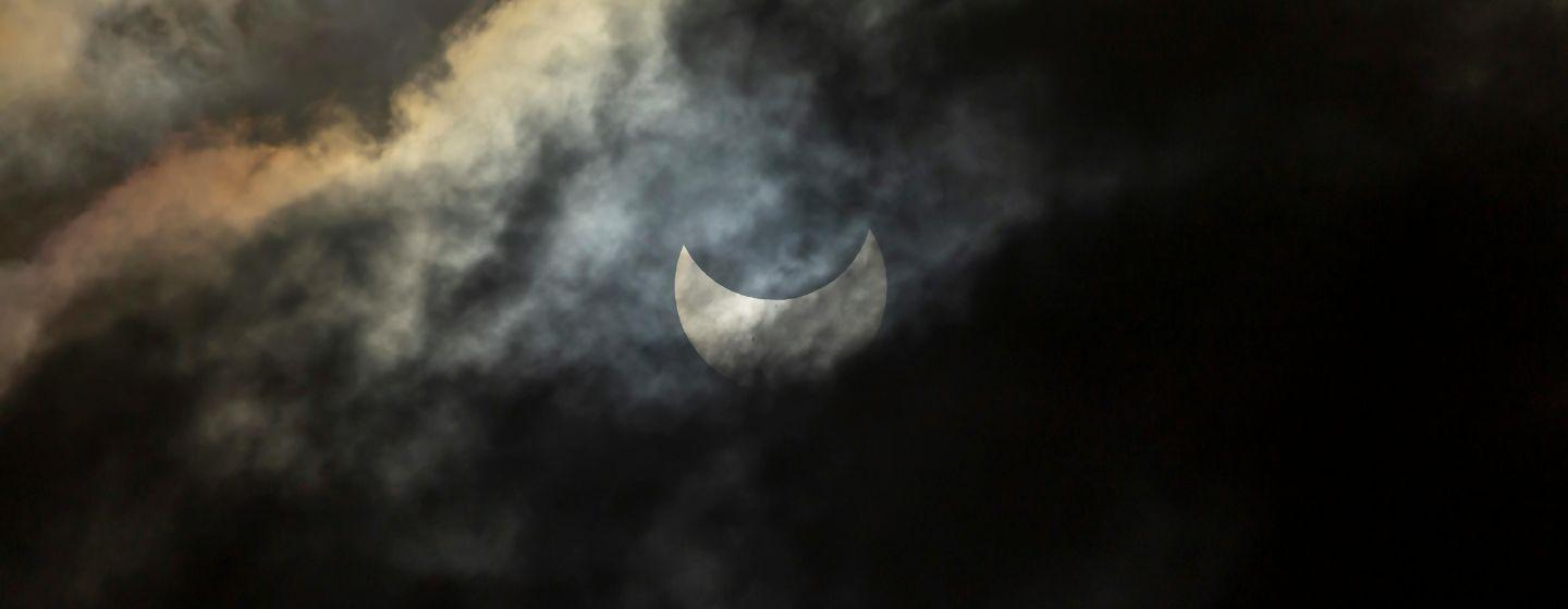 A partially covered stage of a solar eclipse on a cloudy night.