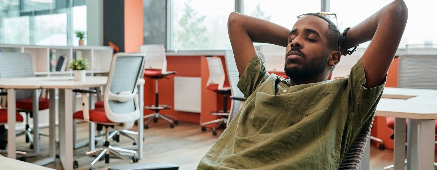 man sitting at desk ar work eyes closed leaning back tired stressed at work, exhausted