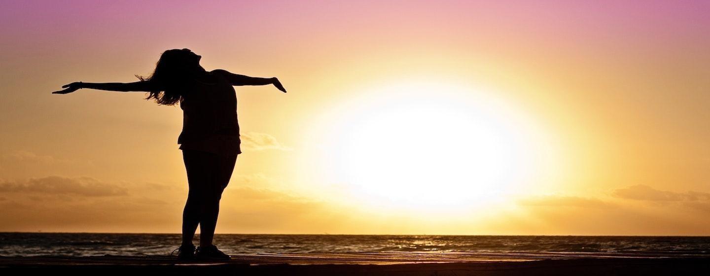 woman on beach sand holding arms out straight to side silhouette on sunset background