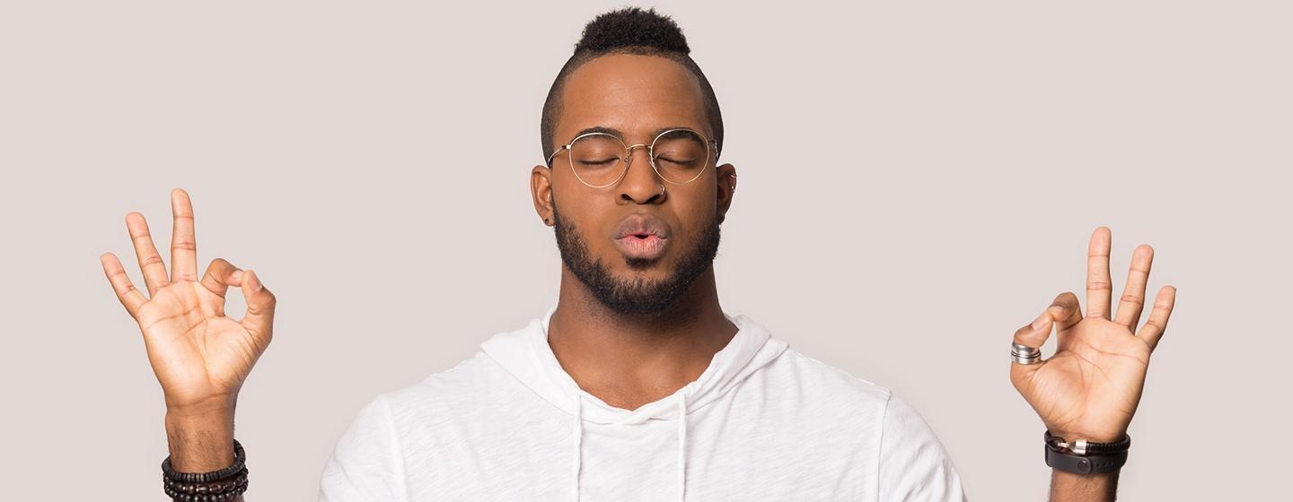 man in white shirt meditating with hands up in ok gesture facing camera with eyes closed slow breathing
