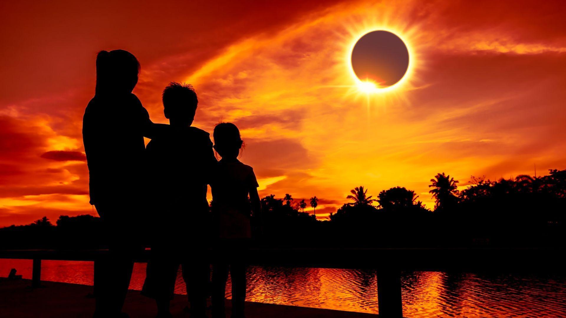 The silhouette of a month and two children watching a total solar eclipse.