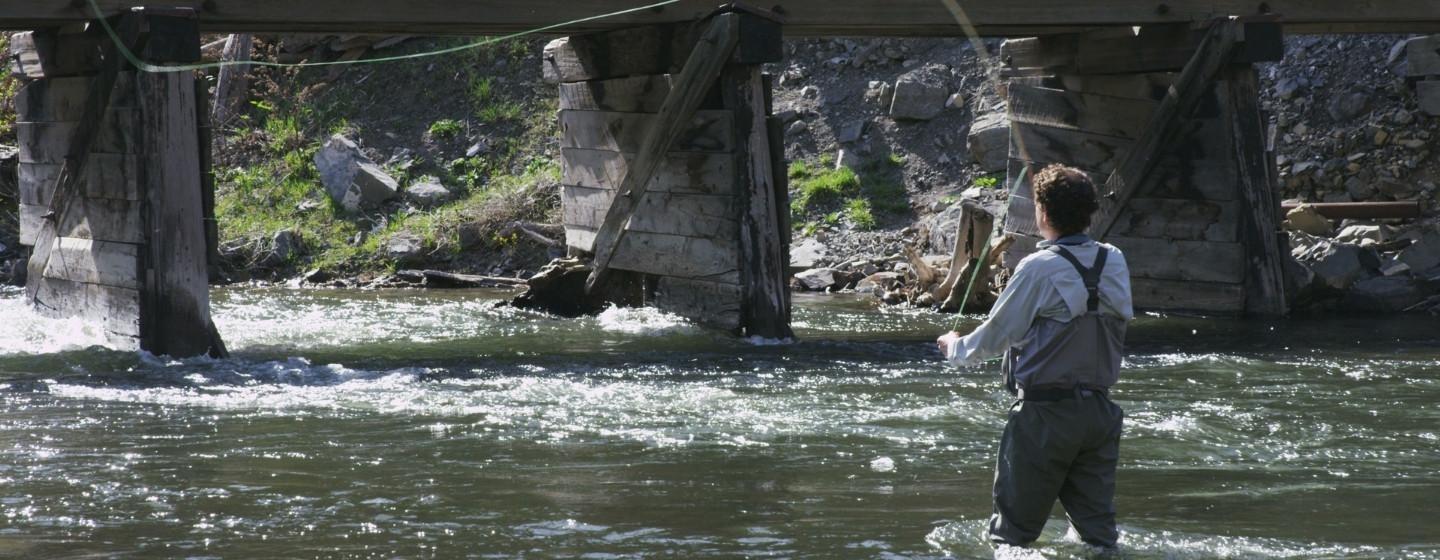 A man fly fishing next to old bridge.